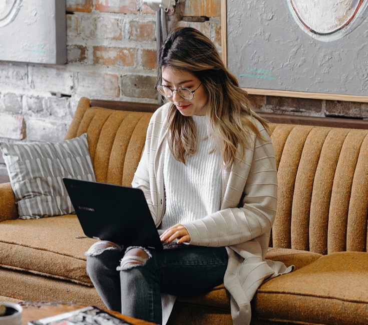 lifestyle image of a woman sitting on a couch and working on a computer